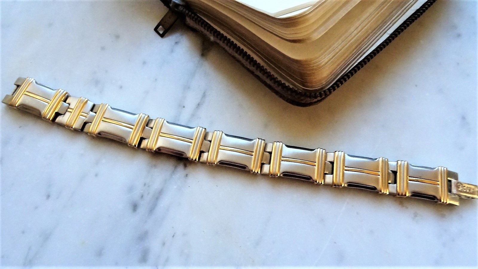 Bracelet bicolore posé sur du marbre à côté d’un livre relié